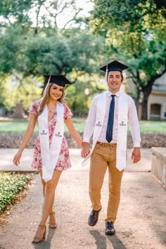 a man and woman in graduation gowns walking down a path holding hands with each other