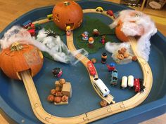 a toy train set with cars and pumpkins on the tracks in a play tray