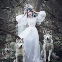 a woman in a white dress standing next to two husky dogs and wearing a tiara