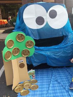 a blue table topped with lots of coins next to a giant cookie tree and an inflatable character