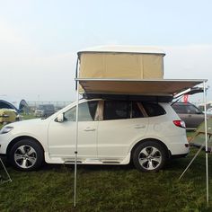 a white car is parked in the grass with its roof open and it's hood up