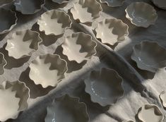 many white dishes are lined up on a gray tablecloth with shadows from the sun