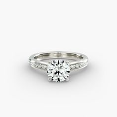 a white gold engagement ring with diamonds on the band and a round brilliant cut center stone