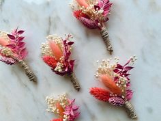 six boutonniers with flowers and feathers on a marble table top in pink, white and orange colors