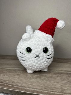 a crocheted white cat with a red santa hat on it's head