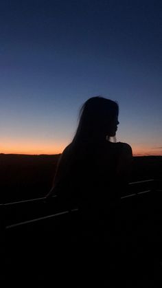 the silhouette of a woman sitting on a bench in front of an orange and blue sky