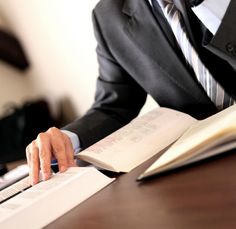 a man sitting at a desk with an open book in front of him and his hand on top of the book