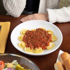 a white bowl filled with pasta and sauce on top of a table next to bread