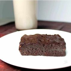 a piece of brownie on a white plate next to a glass of milk