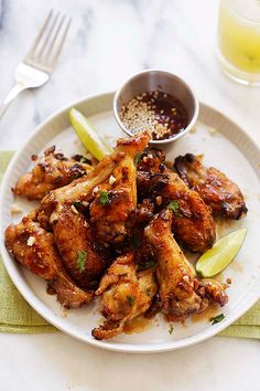 a white plate topped with chicken wings and garnished with lime wedges next to a glass of orange juice