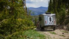 an rv is parked on the side of a dirt road in the woods with mountains in the background