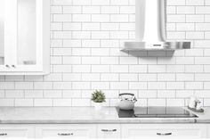 a kitchen with white cabinets and tile backsplash, potted plant on the stove