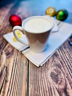 a cup of coffee sitting on top of a white napkin next to christmas balls and candy