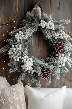 a christmas wreath with white berries and pine cones hanging on a wall next to pillows