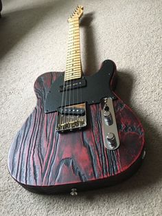 a red and black guitar laying on the floor with it's neck resting up