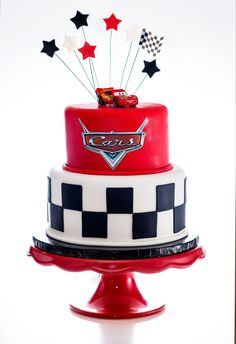 a red and white cake with cars on top is sitting on a pedestal in front of a white background