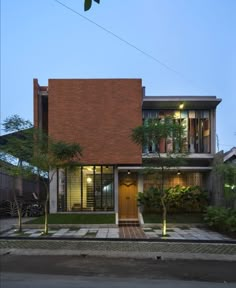 the house is surrounded by greenery and trees at night, with its lights on