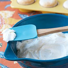 a blue bowl filled with white frosting next to muffins