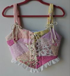 a pink and yellow patchwork top hanging on a wooden hanger next to a white wall