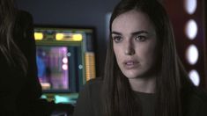 a woman with long hair standing in front of a computer screen and looking at the camera