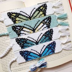 three bookmarks with butterflies on them and tassels hanging from the pages in front of an open book