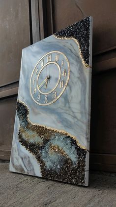 a clock that is sitting on the ground next to a door with it's face covered in black and gold paint