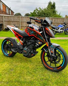 an orange and black motorcycle parked on top of a lush green field next to a wooden fence