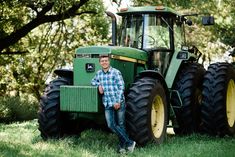 a man standing next to a green tractor in the middle of a grass covered field