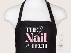 the nail tech apron is black and has pink letters on it that read,'the nail tech '