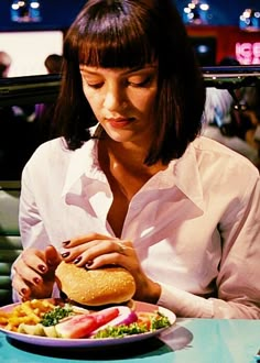 a woman sitting at a table eating a hamburger