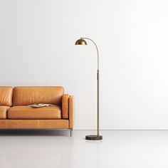 a brown leather couch sitting next to a tall metal lamp on top of a white floor