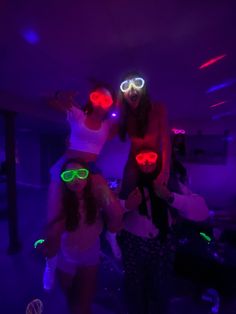 two girls wearing neon goggles in a room with purple lights and one girl has her arms around the other