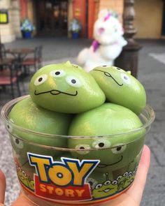 a person holding up a plastic cup filled with toy story green eggs in front of a building