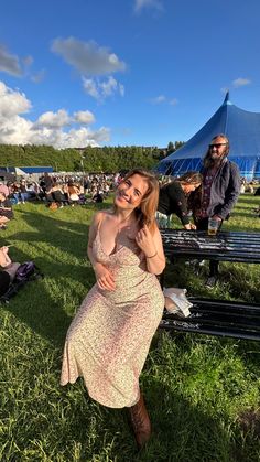 a woman in a dress sitting on a bench at an outdoor event with other people