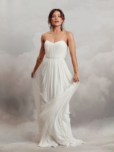 a woman in a white dress standing on a cloud filled sky with her eyes closed