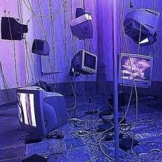 several televisions and wires are tangled up in a room with purple lighting on the walls