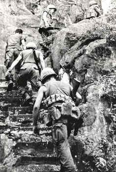 black and white photo of soldiers climbing stairs in the mountains, with backpacks on their backs