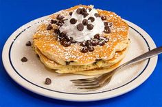 a stack of pancakes topped with chocolate chips and whipped cream on a white plate next to a fork