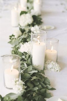 a long table with candles, flowers and greenery on the top is decorated in white