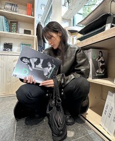 a woman sitting on the floor reading a book in front of a bookshelf