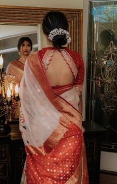 a woman standing in front of a mirror wearing a red and white sari