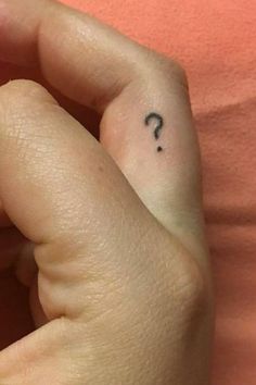 a woman's hand with a small tattoo on her left thumb and a question mark in the middle