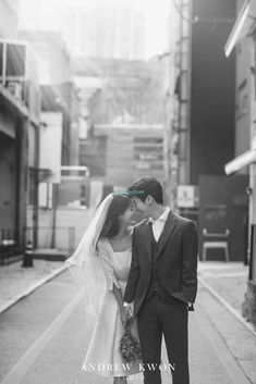 a bride and groom kissing on the street in front of some buildings, black and white photo