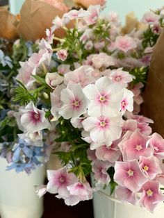 some pink and blue flowers in white vases on a table with brown paper bags