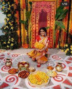 a woman sitting in front of a decorated stage with food on the floor and decorations around her