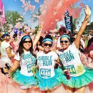 three girls in tutu skirts are throwing colored powder at the camera