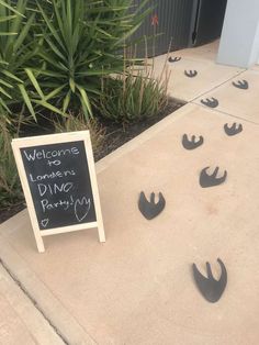 a sign that is on the side of a building near some plants and grass with footprints in front of it