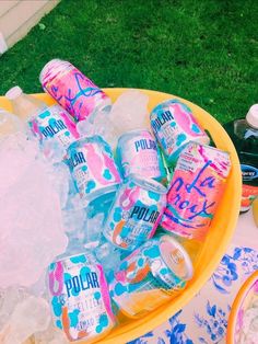 an ice bucket filled with lots of pink and blue soda cans sitting on top of green grass