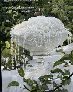 a white vase with pearls and beads on top of a table in front of trees