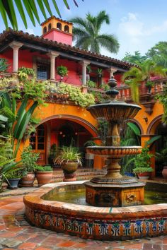 a fountain surrounded by potted plants in front of an orange and red building with palm trees